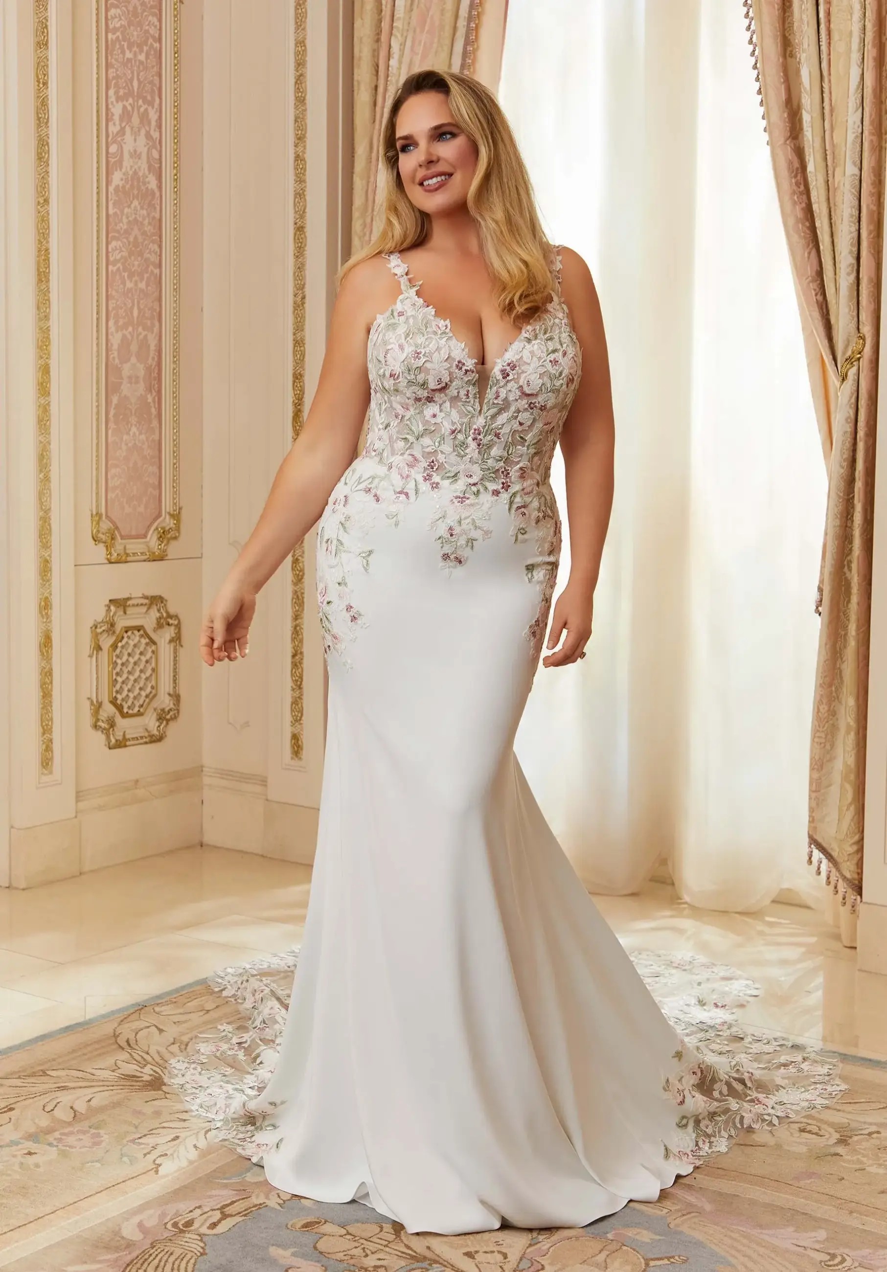 Model is wearing a plus size fit and flare bridal gown with straps and plunging neckline
