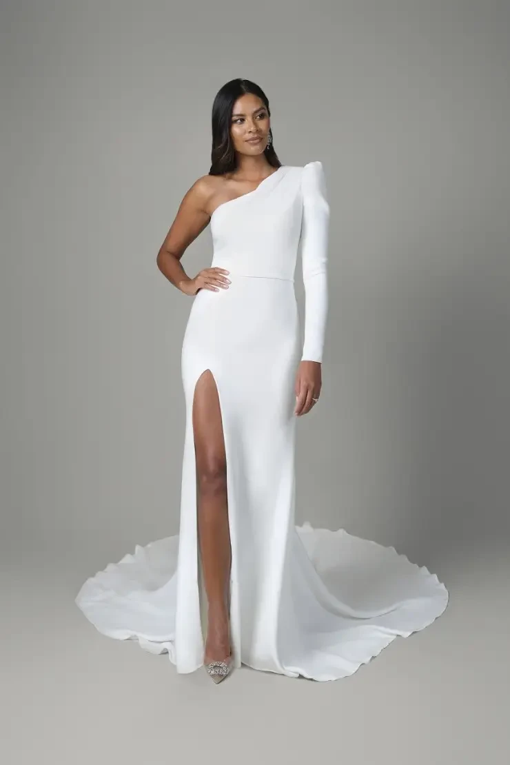 A modern column gown with clean fabric, a structured one-shoulder sleeve, and a high slit for minimalist, fashion-forward brides.