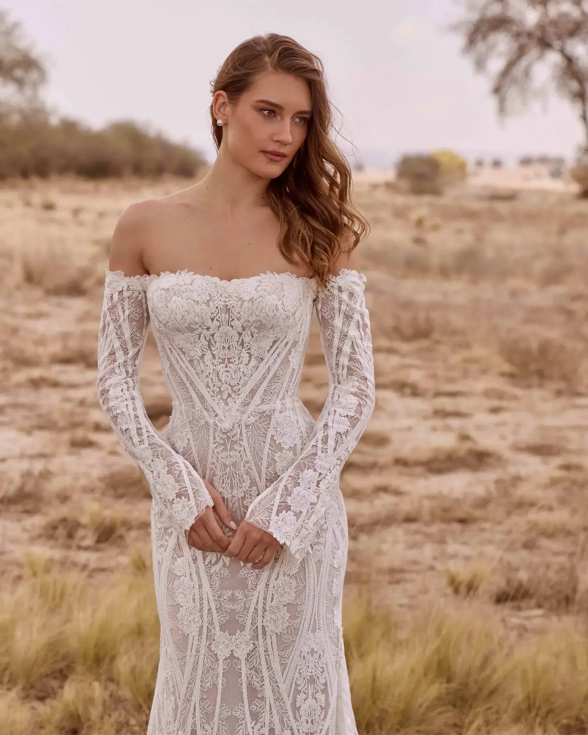 Model is wearing a strapless or off-the-shoulder boho lace wedding dress with a corseted bodice, soft lace paneling, and detachable sleeves.