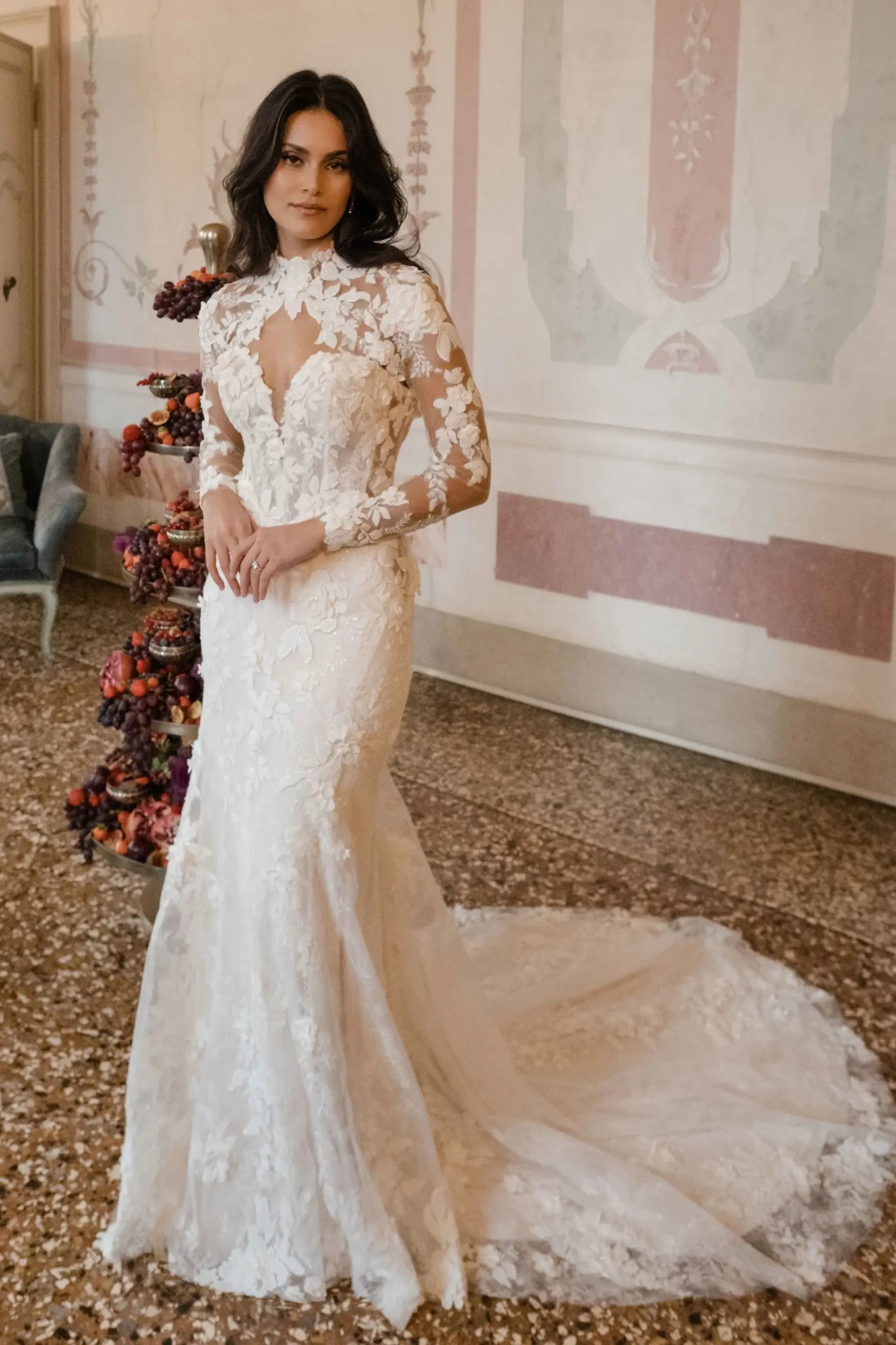 A woman wearing an elegant white wedding dress with intricate lace details, standing gracefully in a beautifully decorated room.